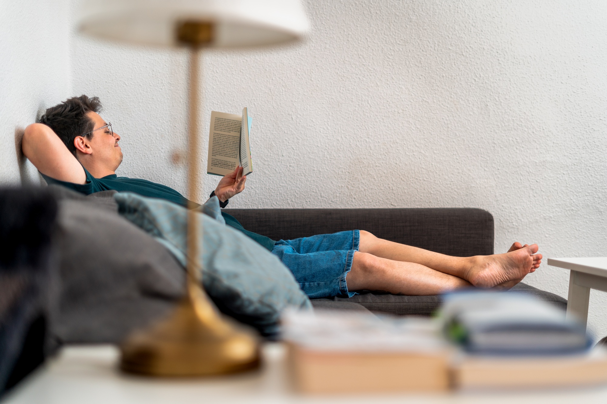 Man relaxing on sofa reading a book at home.